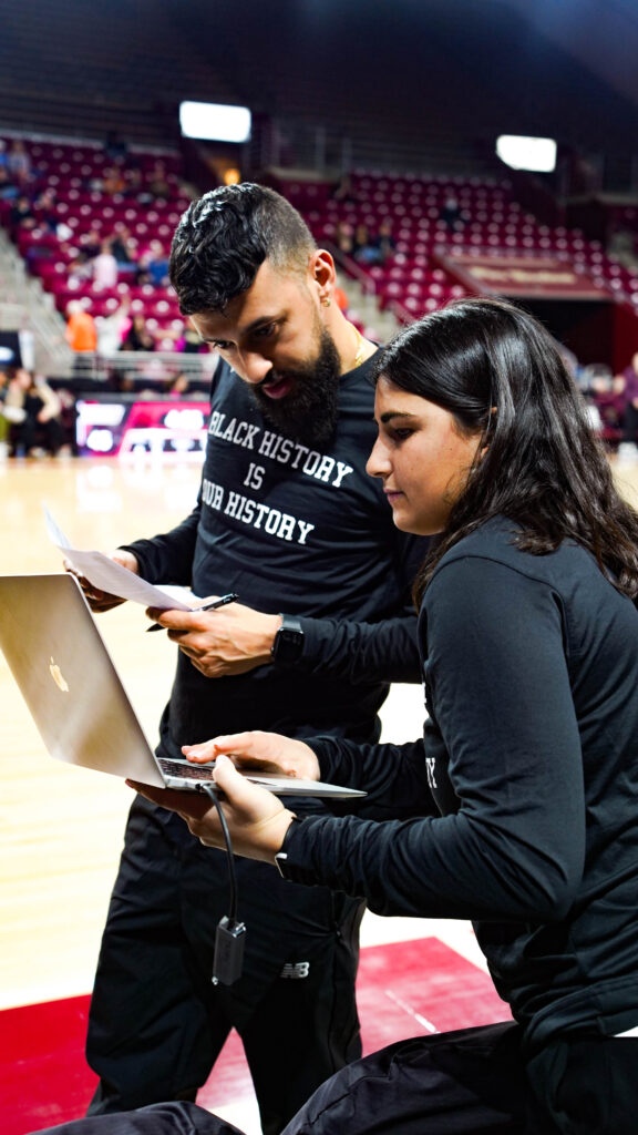 DERRICK SLAYTON, COORDINADOR DE VIDEO EN BOSTON COLLEGE WBB y el personal discuten estrategias en la cancha, con una computadora portátil que muestra el software Catapult Pro Video Focus en primer plano. Esta imagen captura la esencia de cómo el flujo de trabajo desde el vivo hasta la banca facilita ajustes inmediatos en el tiempo de juego y planificación estratégica.