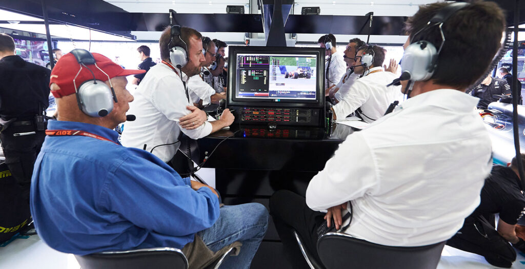 
A team of Formula 1 engineers and strategists intensely monitor live race data and video feeds on computer screens at the team's command center during a Grand Prix.