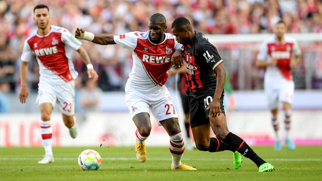 Two male football players in a duel for the ball during a competitive match, with one in a red and white kit and the other in black and red