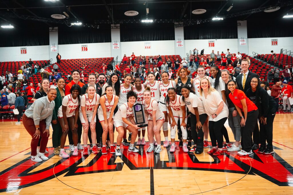 The UNLV Lady Rebels Women's Basketball team proudly gathered on the court, smiling and posing with a championship trophy, exemplifying the team spirit and success that can be achieved through effective use of video analysis and strategic development.