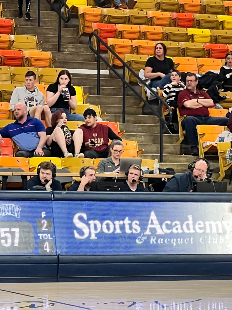 Un public ciblé est capturé dans les tribunes d'une arène de basket-ball, avec un groupe d'individus engagés dans une conversation, symbolisant les efforts de collaboration dans les discussions stratégiques qui sont cruciales pour le développement de l'équipe et l'analyse du jeu.