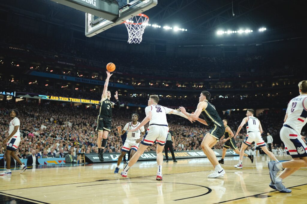 在挤满人的体育场内，一名普渡锅炉工队篮球运动员在比赛中半空中投篮。