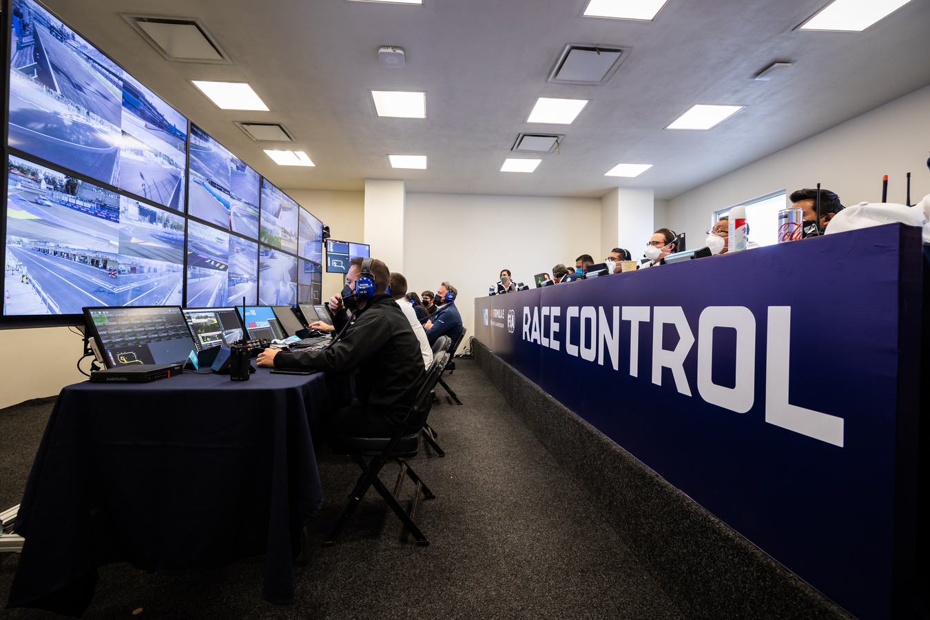 Two rows of stewards in Race Control analysing data and video screens