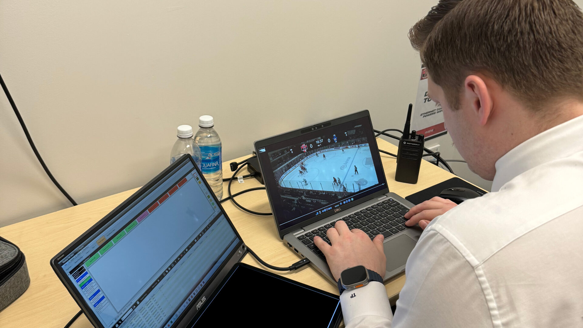 A focused hockey coach analyzing live game footage on a laptop at the rink.