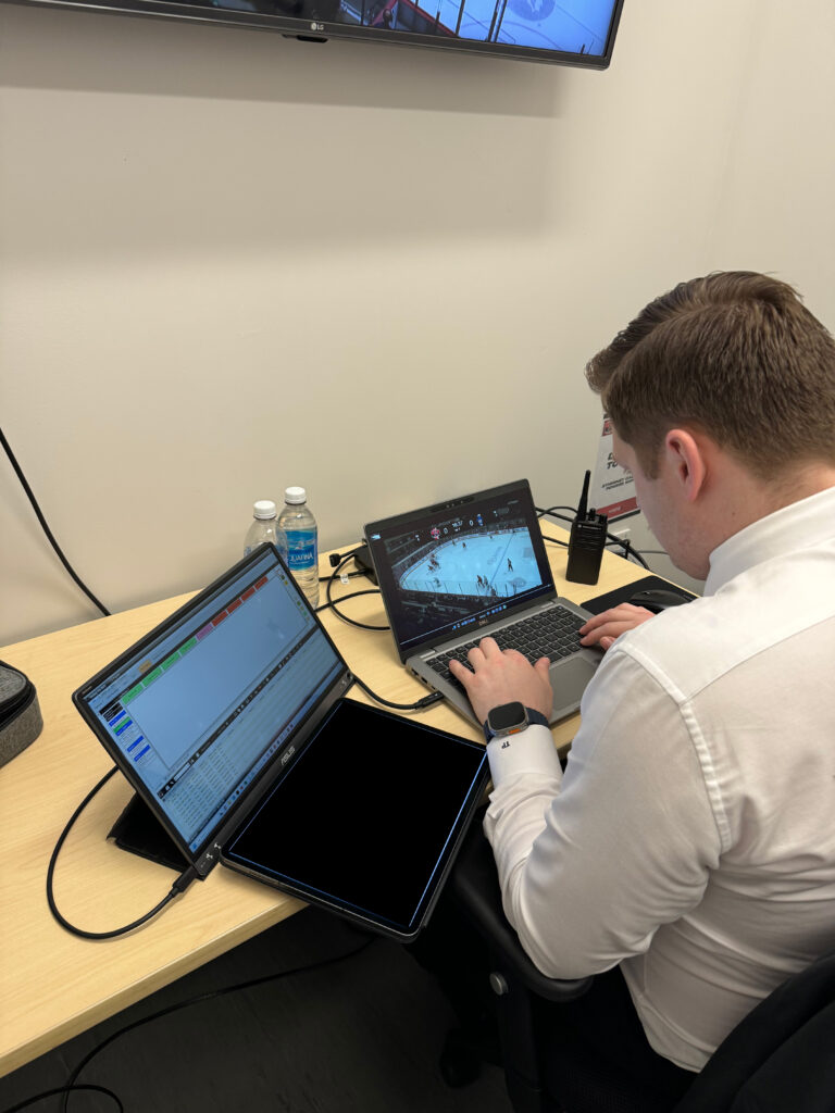 A focused hockey coach analyzing live game footage on a laptop at the rink.