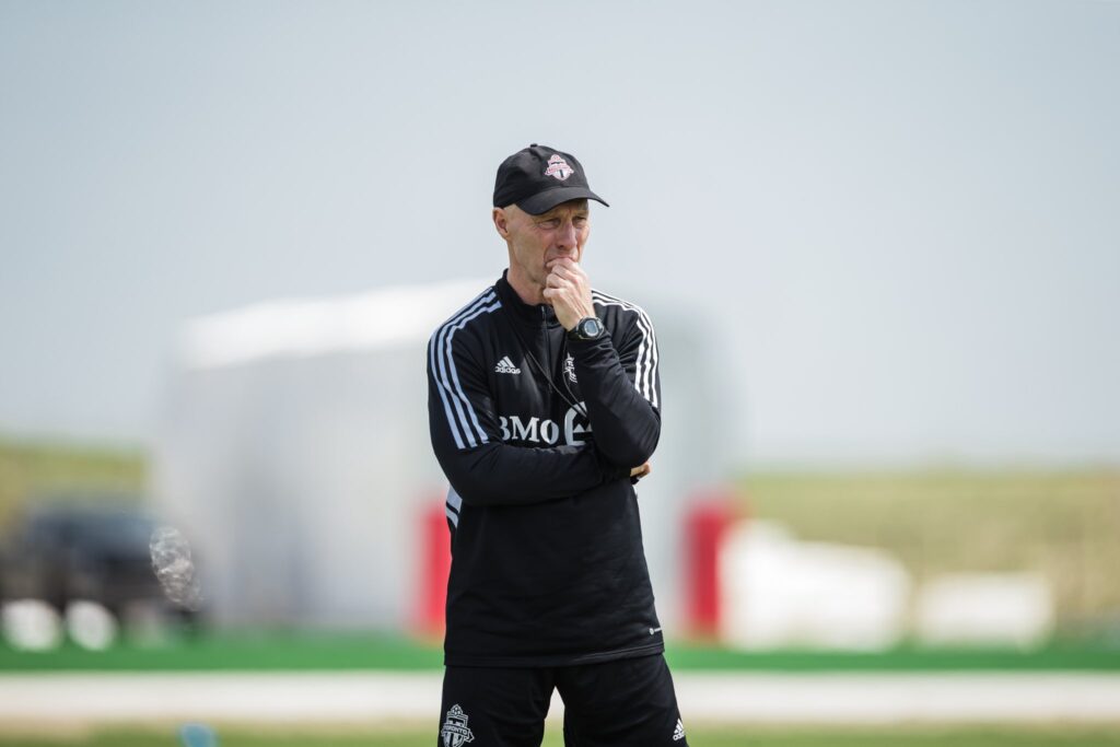 Ein Trainer, gekleidet in einen schwarzen Trainingsanzug des Toronto FC, beobachtet die Spieler nachdenklich während einer Trainingseinheit.