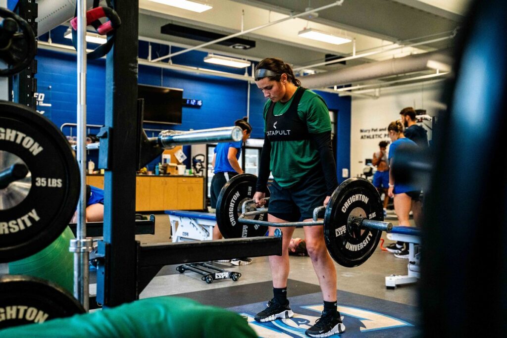 นักฟุตบอลหญิงของ Creighton กำลังทำท่าเดดลิฟต์ในโรงยิม โดยสวมเสื้อกั๊กติดตามของ Catapult เพื่อติดตามข้อมูลการฝึกความแข็งแรง