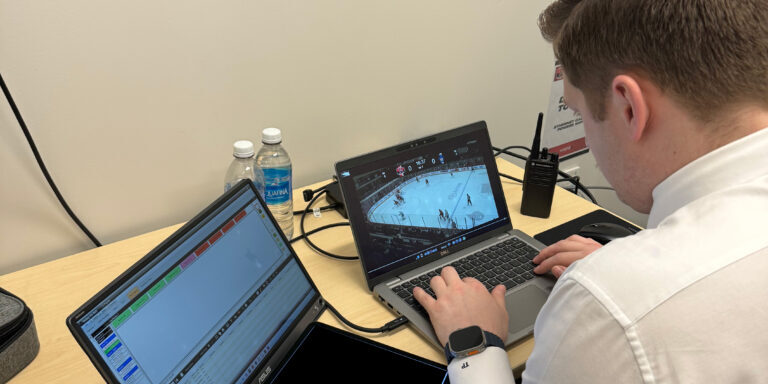 A focused hockey coach analyzing live game footage on a laptop at the rink.